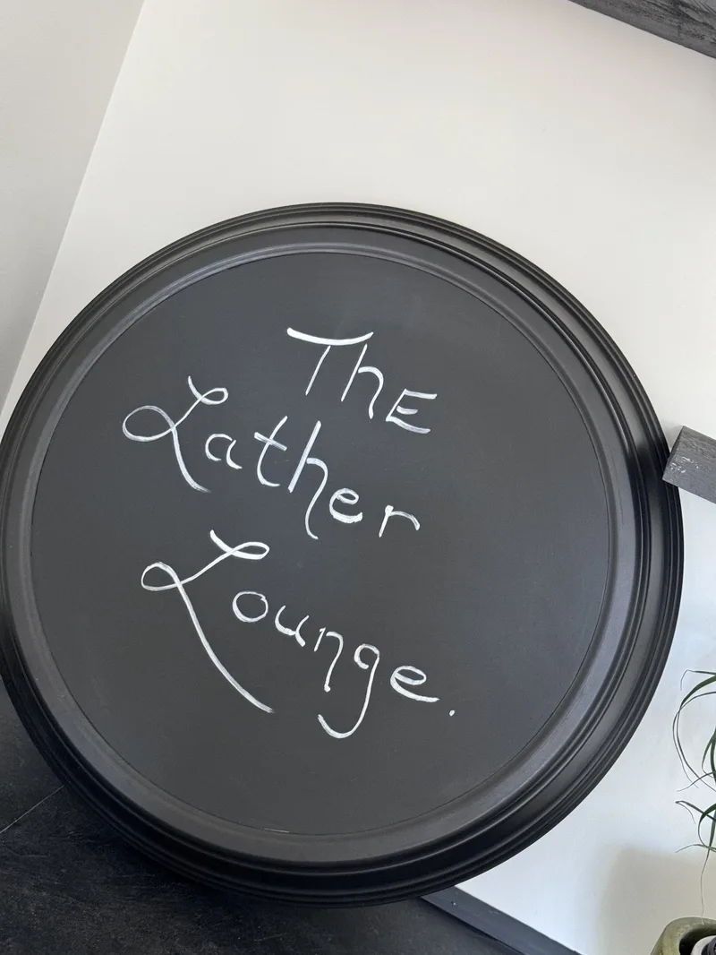 The Lather Lounge sign, handwritten on a round black tray